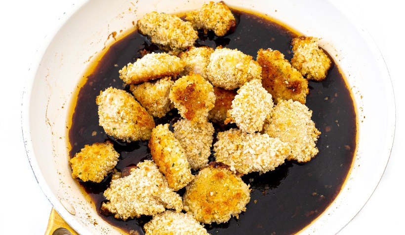 adding breaded chicken pieces to honey sriracha sauce in pan